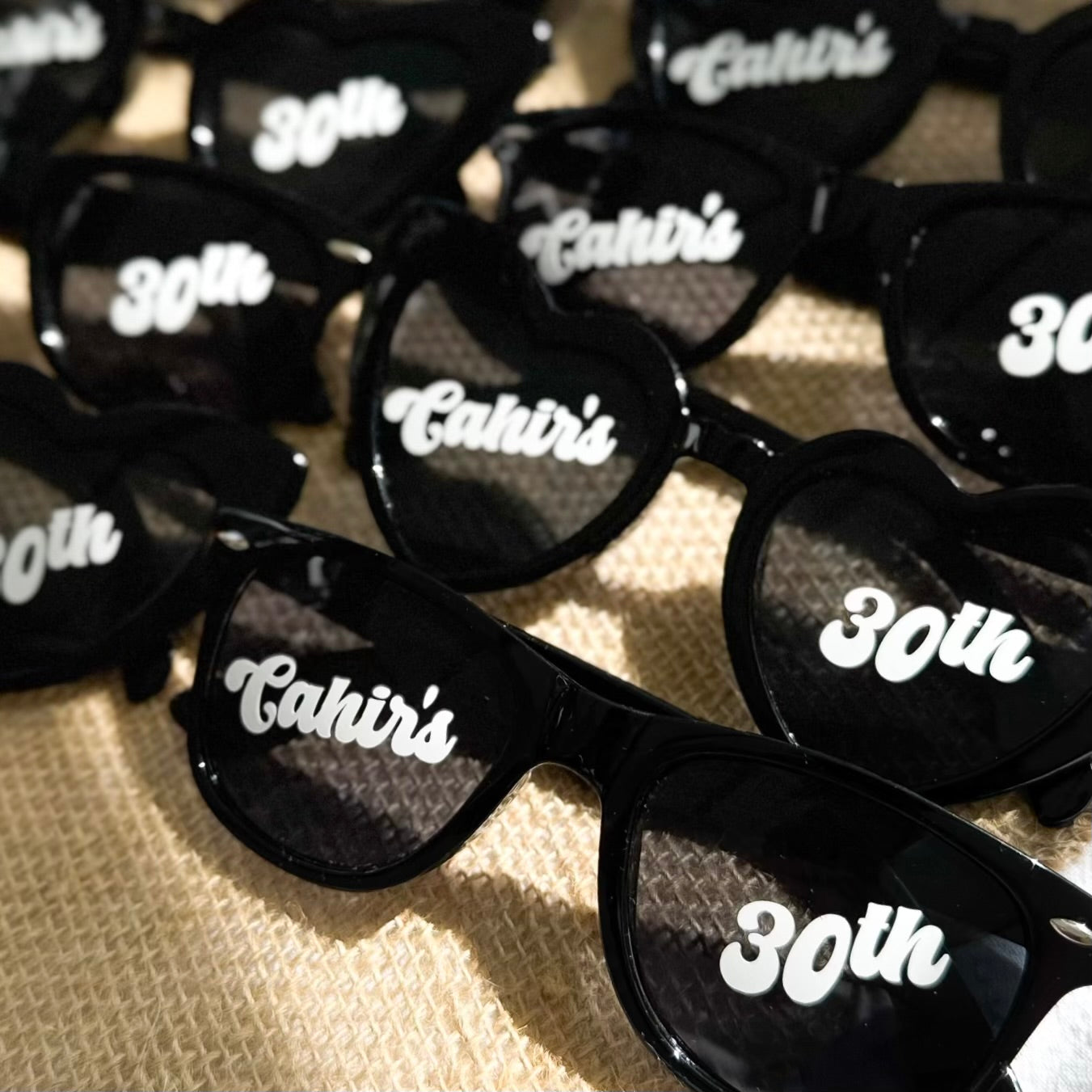 Black sunglasses with 'Cahir's' and '30th' text on a textured surface