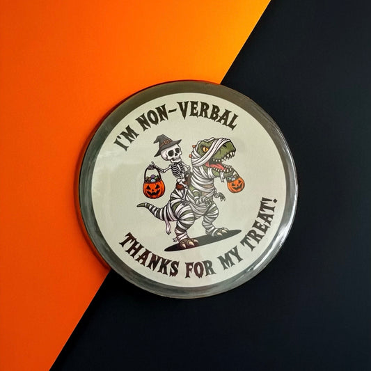 Round Halloween dinosaur pin badge with cartoon dinosaur and skeleton green background, text reads ‘I’m non-verbal, thanks for my treat’