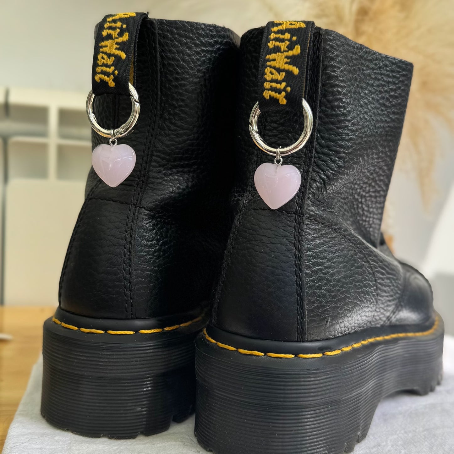 Black leather boots with yellow stitching and heart-shaped charms on a neutral background