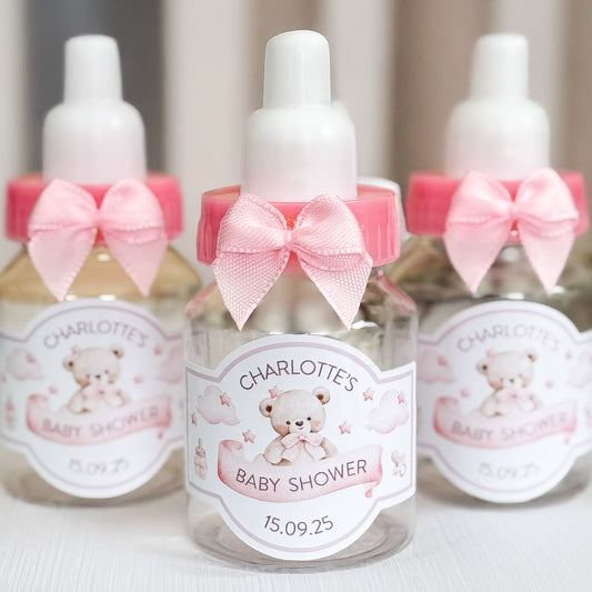 Small bottles with pink bows and personalised labels for a baby shower.
