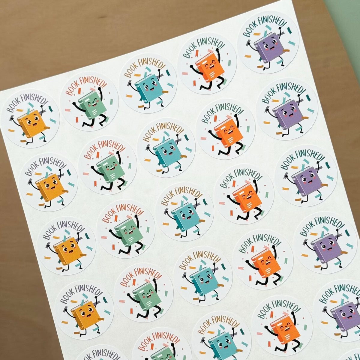 Teacher-friendly sticker sheet with cartoon characters holding books and ‘Book Finished’ text on wooden surface