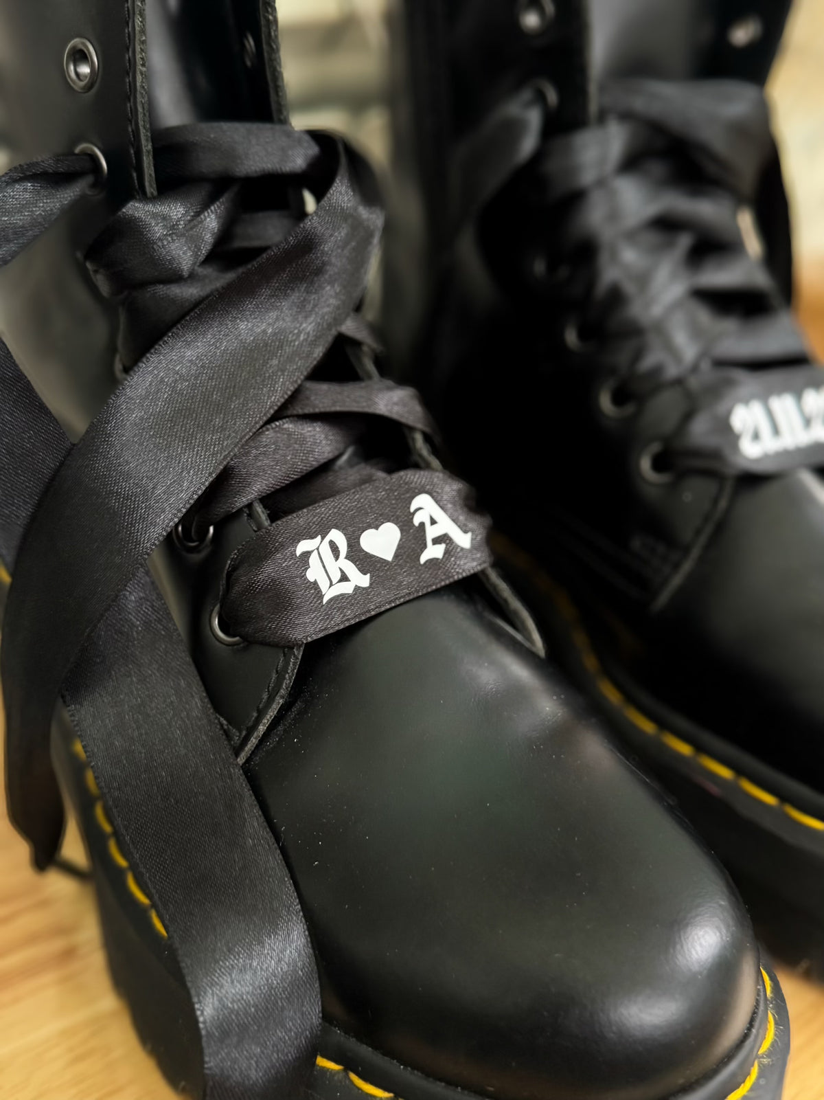 Custom black satin bridal boot laces printed with couple’s initials and wedding date, styled on lace-up Dr. Martens.