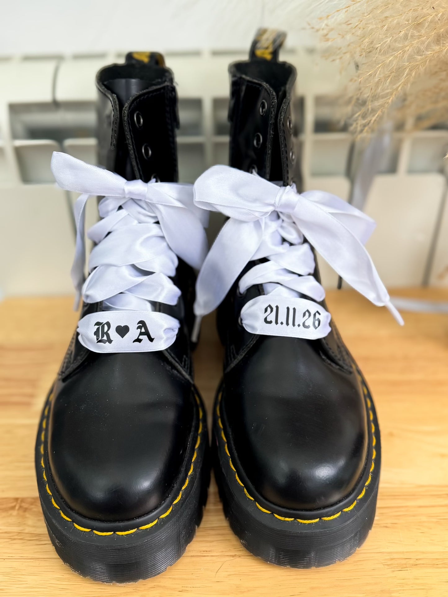 White satin personalised wedding shoelaces with initials and date, laced through black Dr. Martens boots and tied into soft bridal bows.