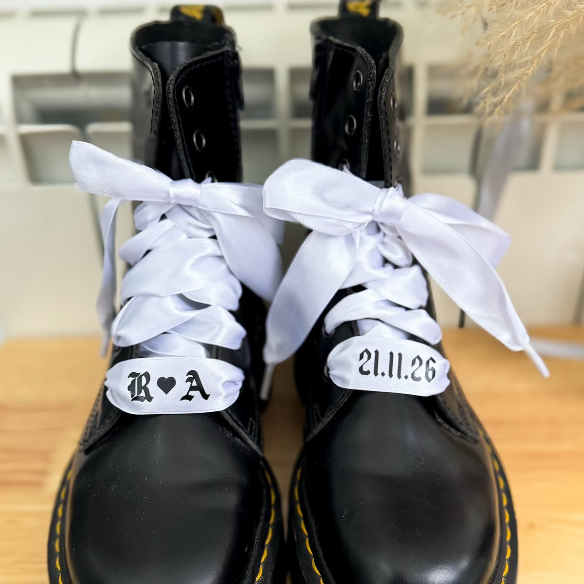 White satin personalised wedding shoelaces with initials and date, laced through black Dr. Martens boots and tied into soft bridal bows.
