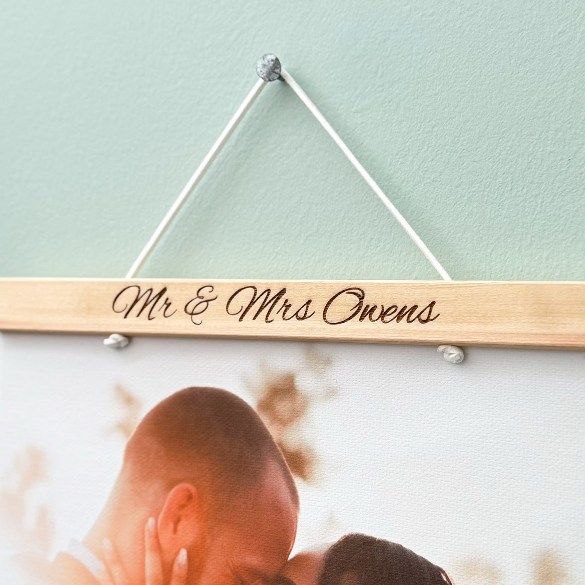 Wooden sign with 'Mr & Mrs Owens' engraved, hanging against a blurred background of a couple.