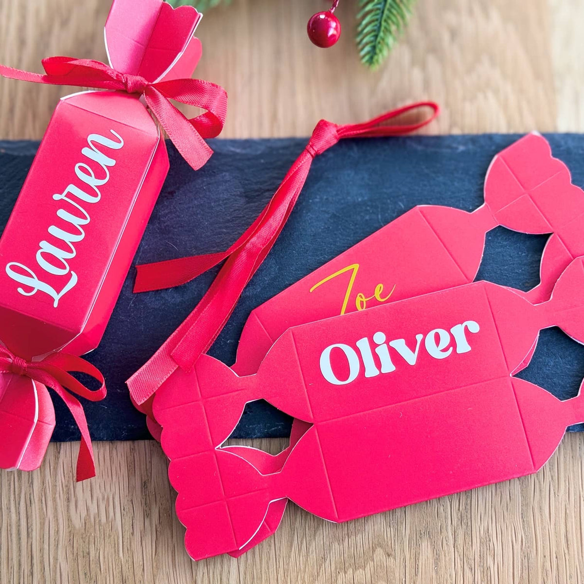 Red Christmas crackers personalised with Lauren, Oliver and Zoe on a dark slate board