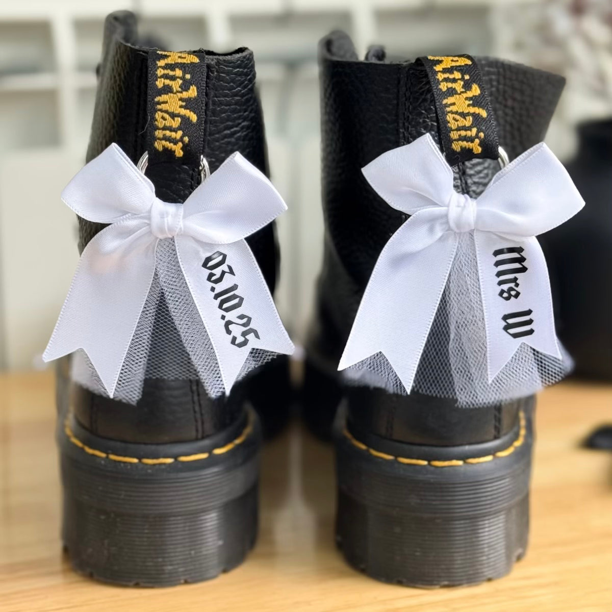 Black boots featuring white ribbons and personalised name and date on wooden surface