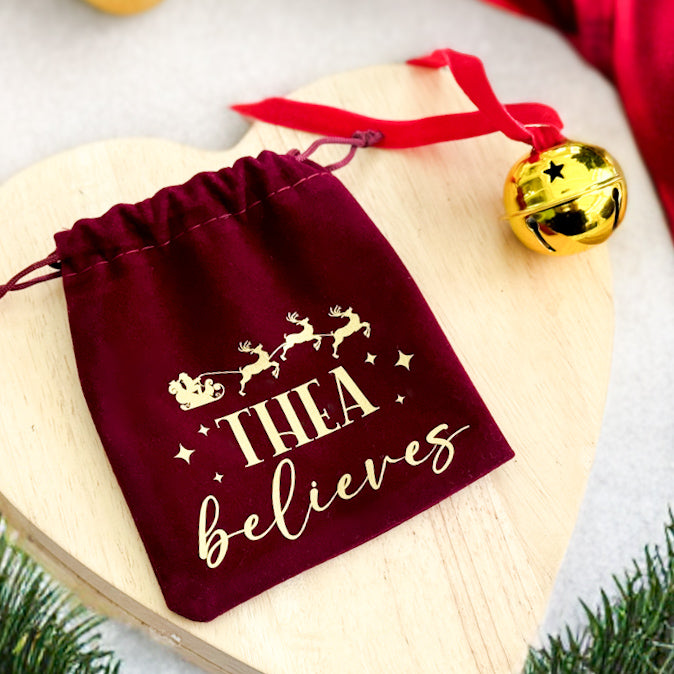 Red velvet Believers Bell bag printed with "Thea believes" beside a gold bell