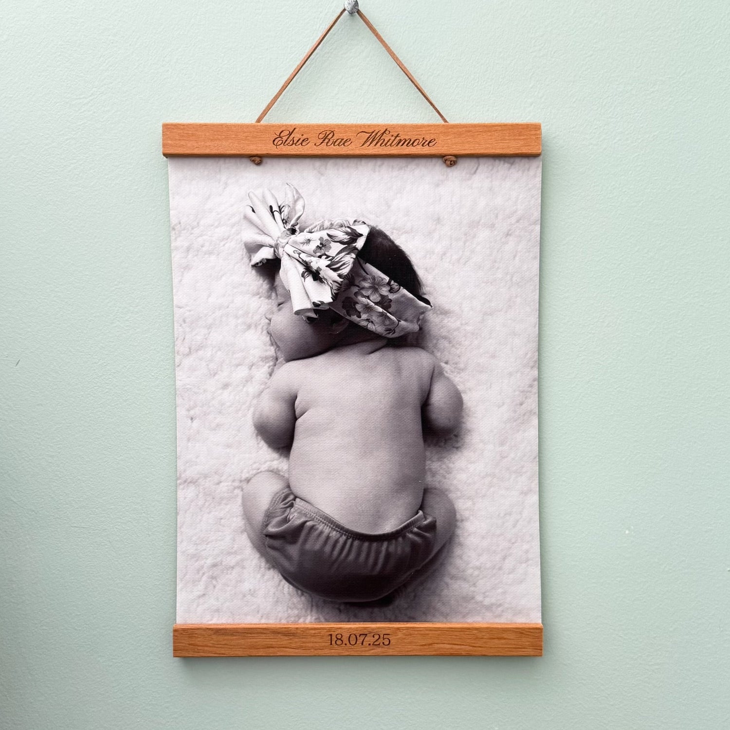 Framed black and white photo of a baby with a wooden frame on a light green wall.