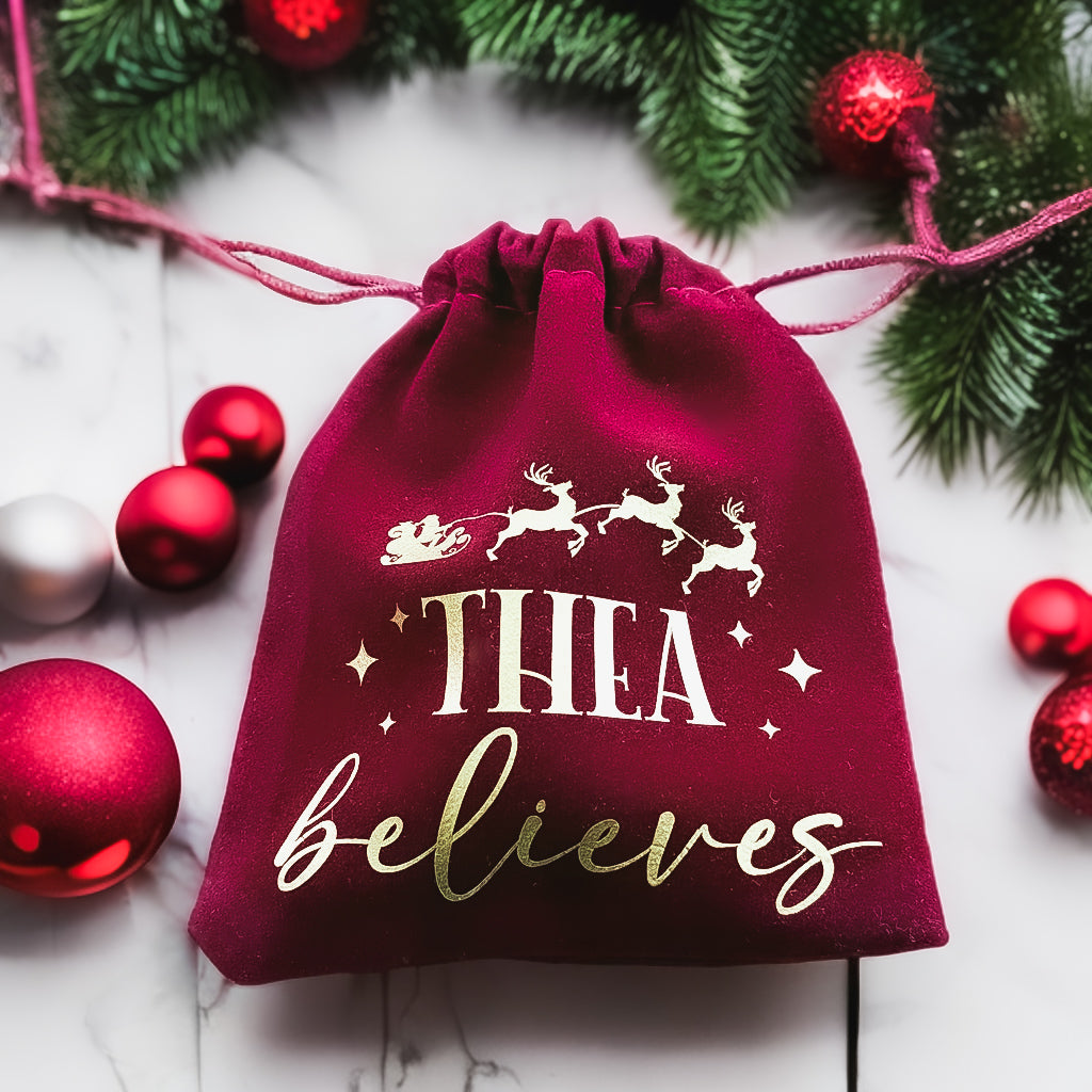Personalised red velvet bag reading "Thea believes" with Santa's sleigh design
