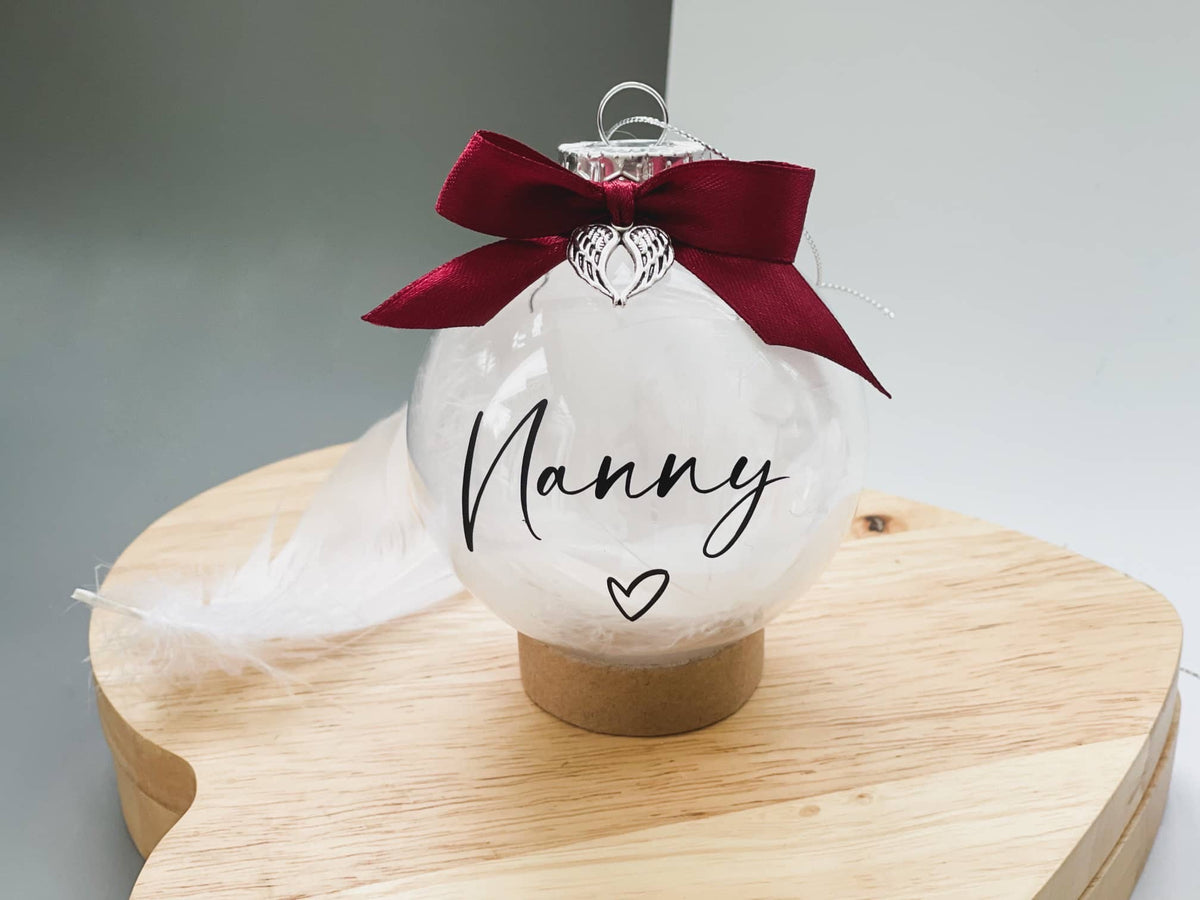 Clear memorial bauble with the name Nanny, a burgundy bow and angel wing charm