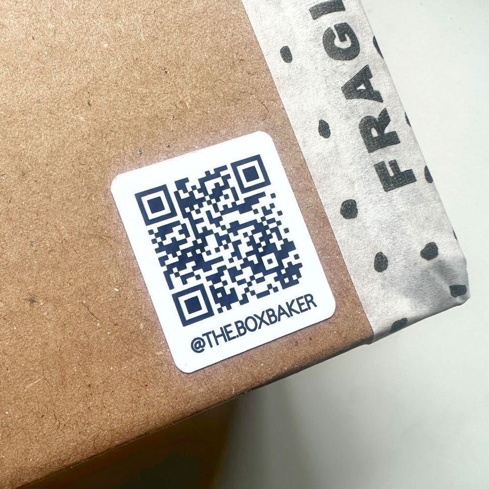 QR code label on a cardboard box with 'The Box Baker' branding.