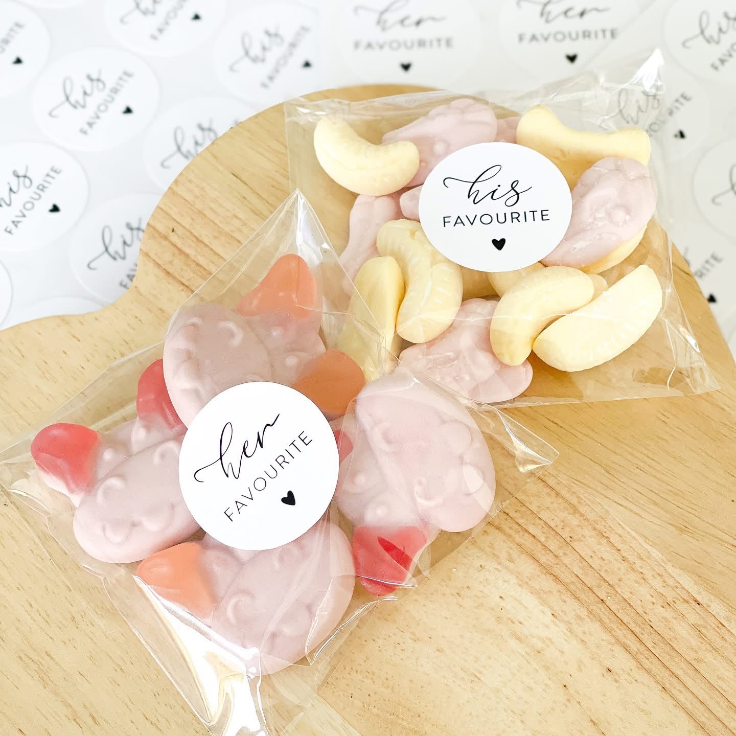Two clear bags of candy with 'Her Favourite' and 'His Favourite' labels on a wooden surface.