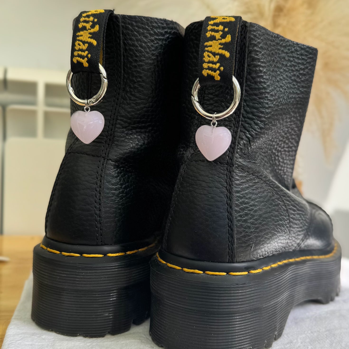 Black leather boots with yellow stitching and heart-shaped charms on a neutral background