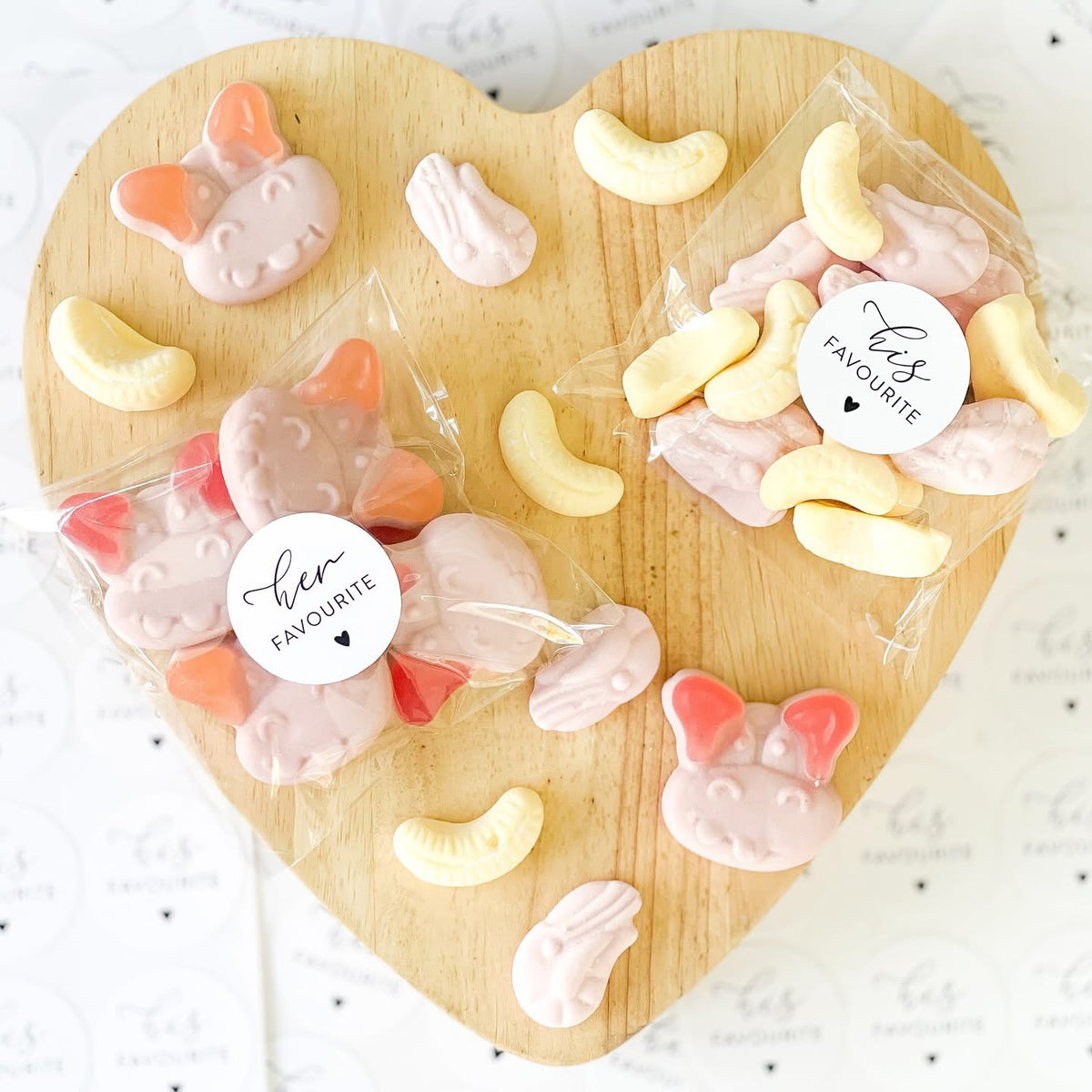 Heart-shaped wooden board with wrapped candy pieces and 'her favourite' labels on a white background