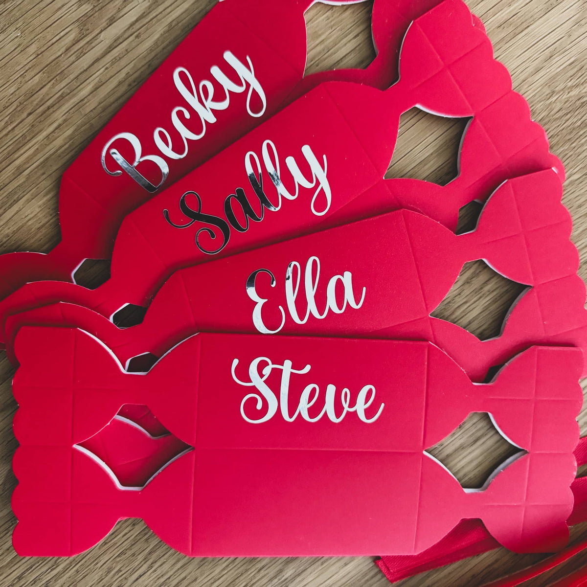 Four flat-packed red DIY Christmas crackers personalised with names in white script