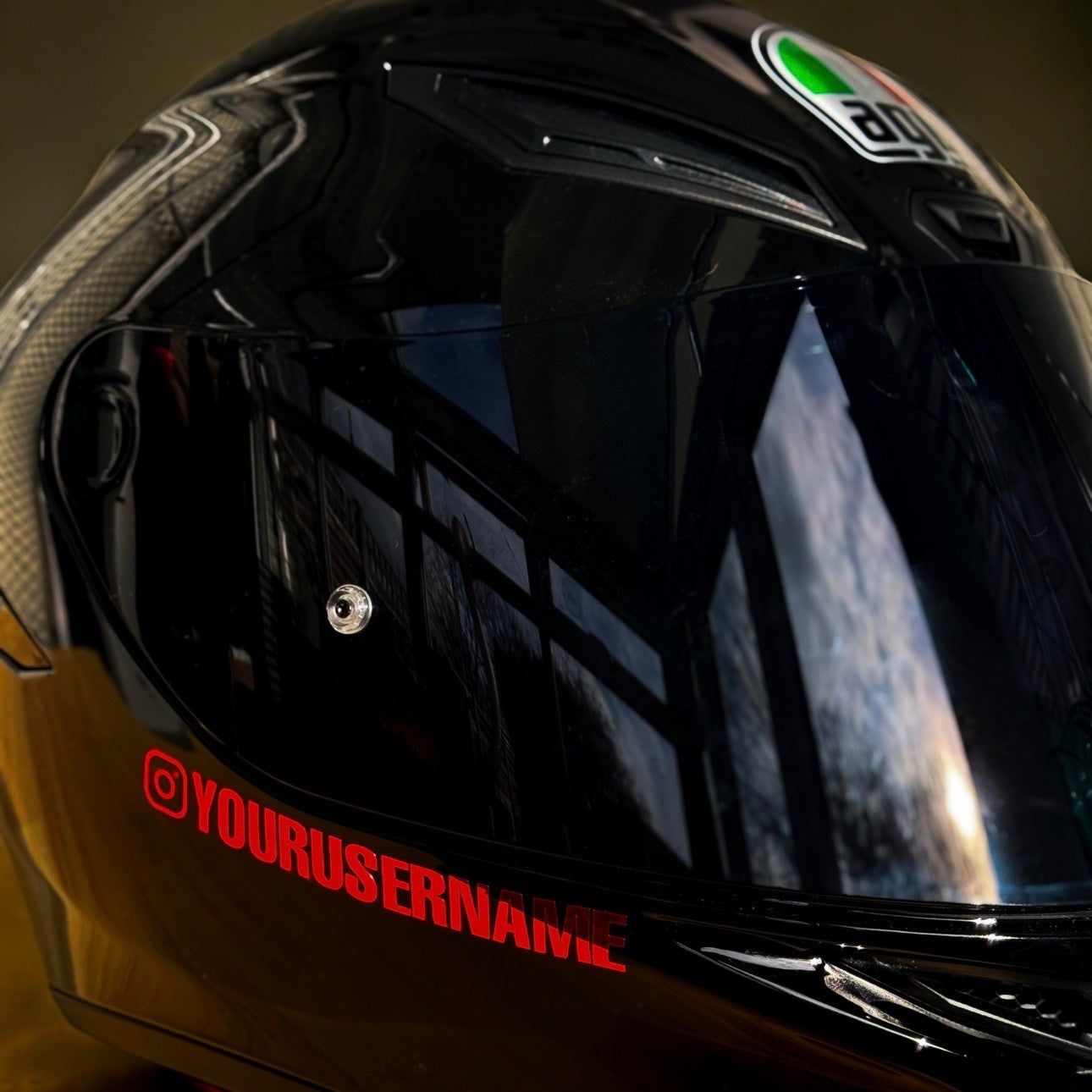 Black motorcycle helmet with reflective visor and branding text on a dark background