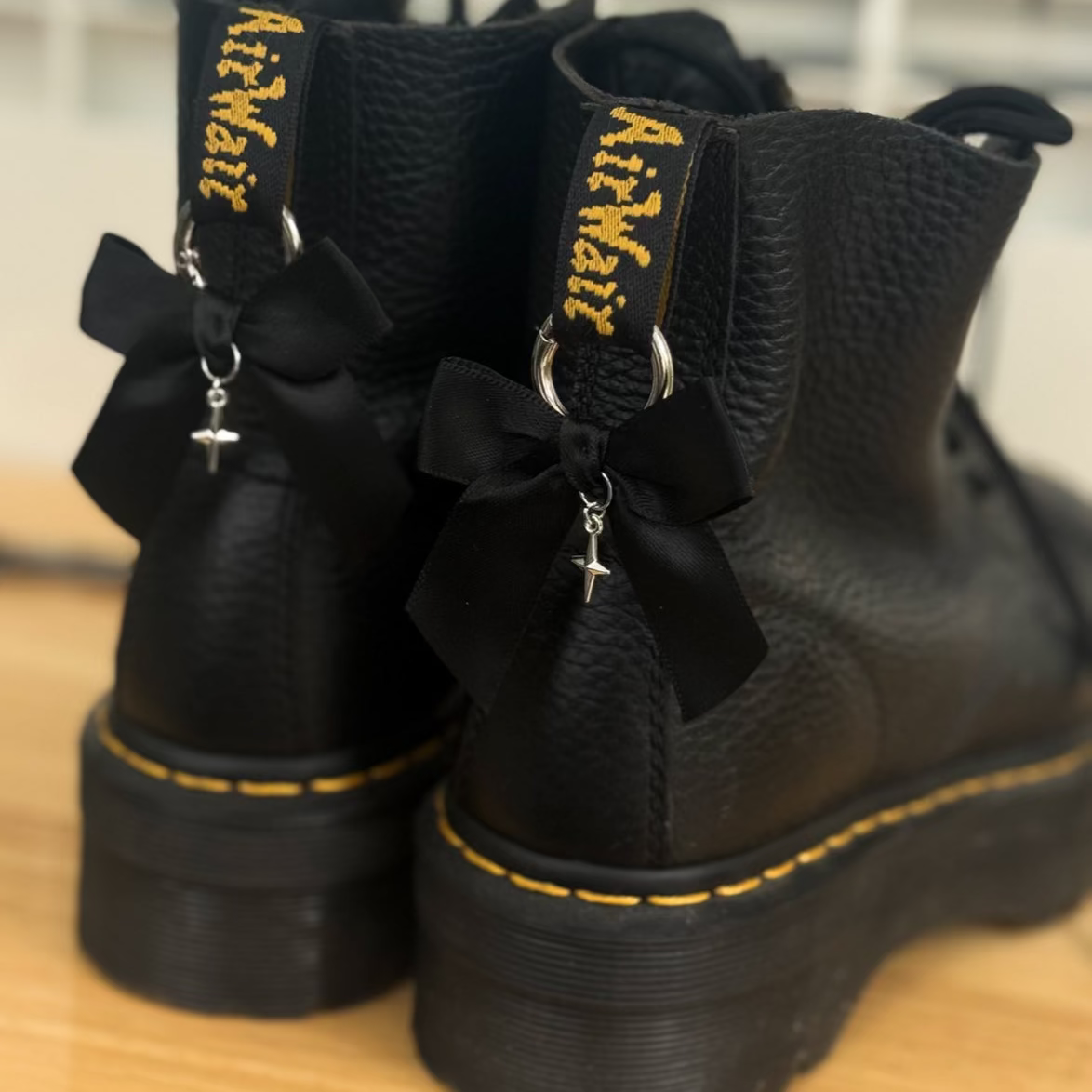 Black boots with yellow stitching and decorative bows on a wooden surface