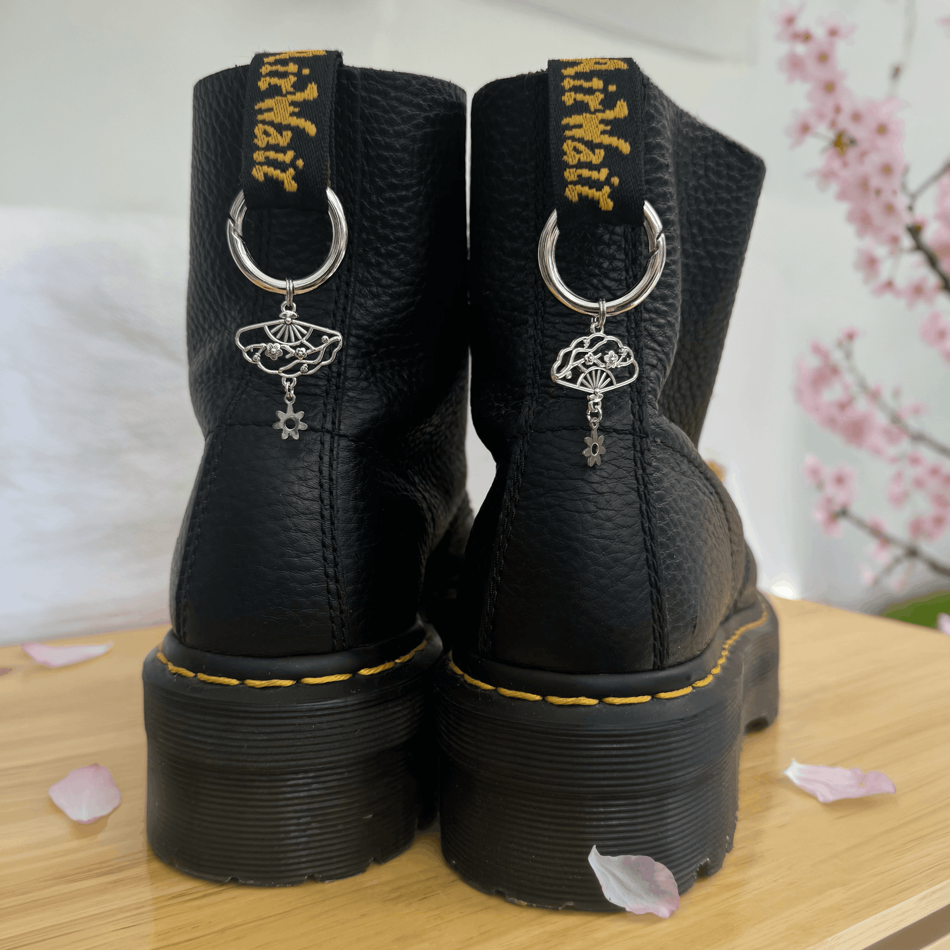 Black boots with decorative charms on a wooden surface with cherry blossoms in the background.