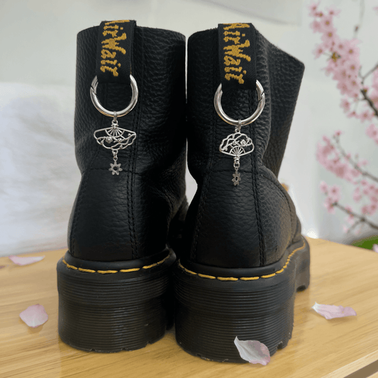 Black boots with decorative charms on a wooden surface with cherry blossoms in the background.