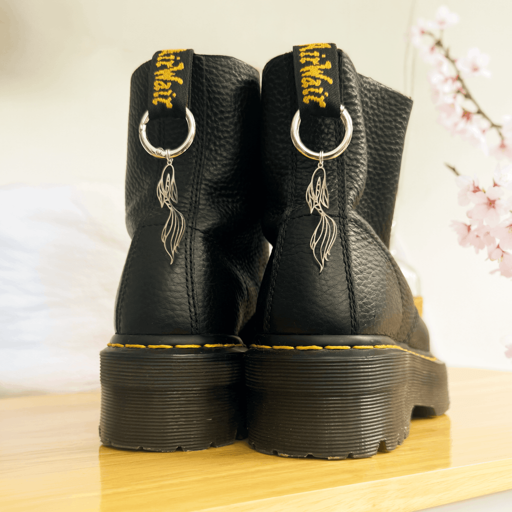 Black boots with unique koi fish charms on a wooden surface