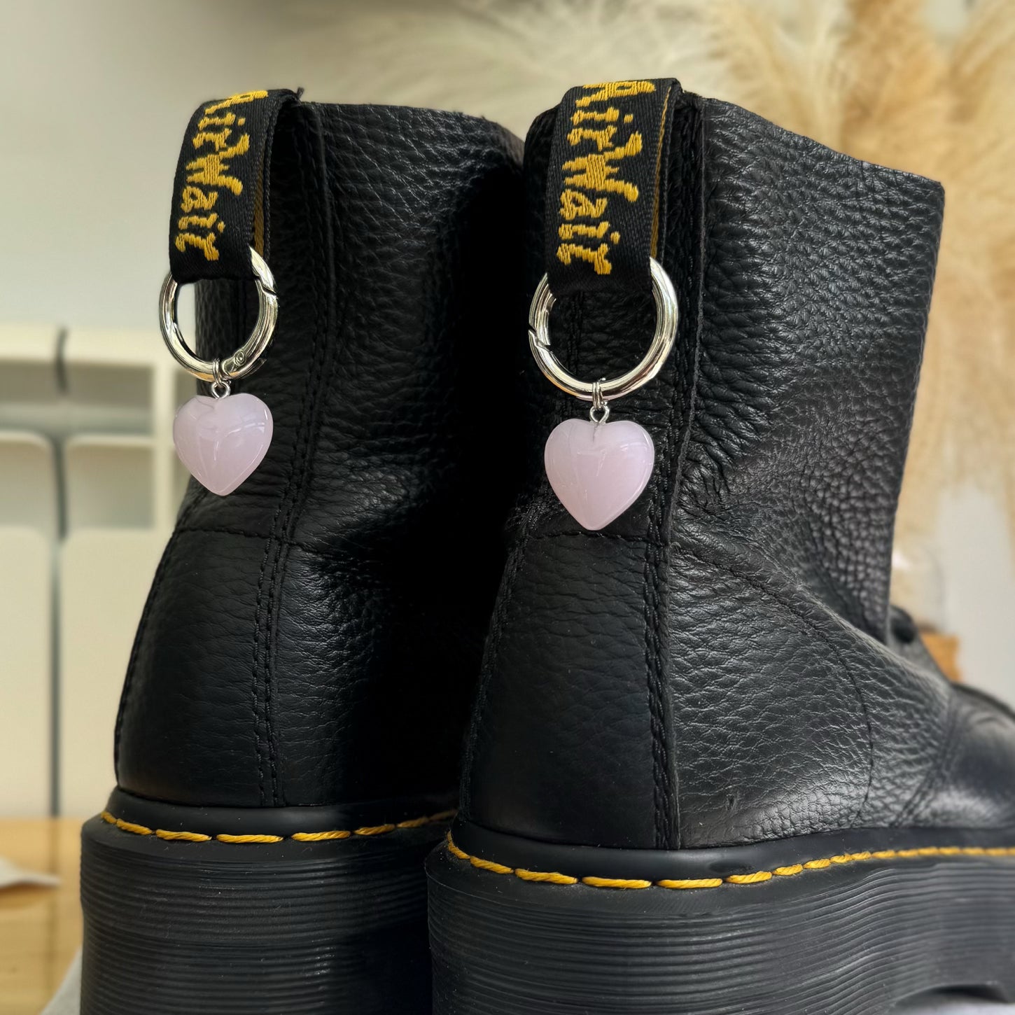 Black leather boots with pink heart charms on the laces against a neutral background