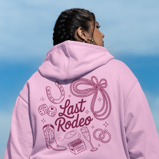 Person wearing a pink hoodie with 'Last Rodeo' design against a blue sky